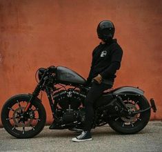 a person sitting on a motorcycle in front of a red wall and wearing a black hoodie