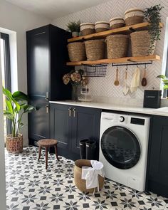 a washer and dryer in a room with black cabinets, white tile flooring and hanging baskets on the wall