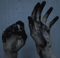 two hands are covered in black paint and one is holding out their hand to the camera