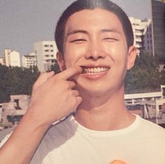 a man holding an orange in his right hand and smiling at the camera with buildings in the background