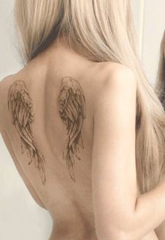 the back of a woman's body with angel wings tattooed on her upper half