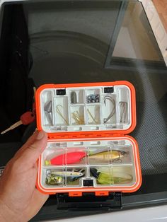 a person holding an orange case filled with different types of fishing lures and hooks