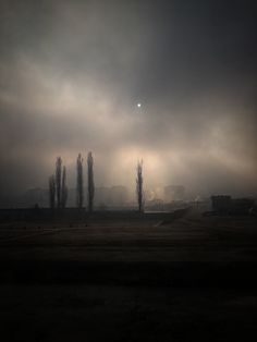 the sun shines brightly through dark clouds over an empty field with trees in the foreground