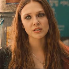 a woman with long hair and green eyes looks at the camera while standing in front of a building