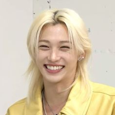 a woman with blonde hair smiling and wearing a yellow shirt in front of a white wall