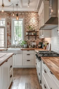 a kitchen with white cabinets and wooden counter tops next to a brick wall that has an open window