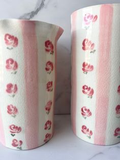 two pink and white vases sitting next to each other on a marble counter top
