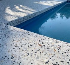 an empty swimming pool in the middle of a concrete patio with gravel and pebbles on it