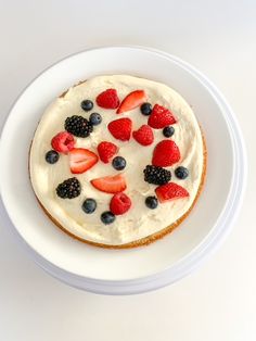 a white plate topped with a cake covered in berries and blueberries on top of it