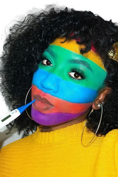a woman with her face painted like a rainbow flag and holding a toothbrush in her mouth