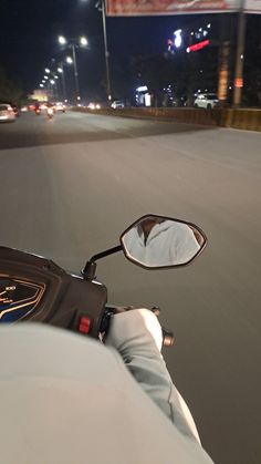 a person riding a motorcycle on a city street at night with their reflection in the side mirror