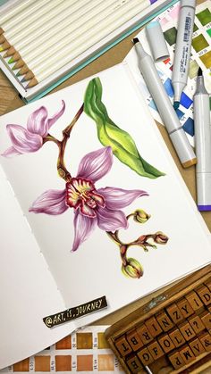 an open book with flowers on it next to some markers and pencils in the background