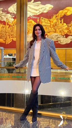 a woman standing in front of a glass wall with her arms out and legs crossed