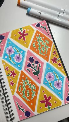 a notebook with colorful designs on it next to a marker and pen, along with two markers