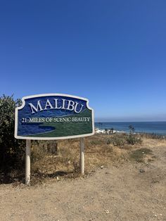 a sign that is on the side of a dirt road near the ocean and some bushes