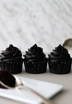 three chocolate cupcakes sitting on top of a table next to a knife and spoon