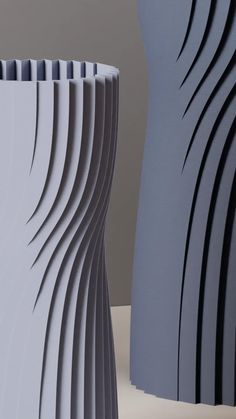 two gray vases sitting next to each other on a white counter top with wavy lines