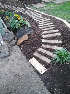 a garden path made out of stones and wood in the middle of a flower bed