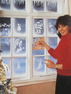 a woman standing in front of a christmas tree holding a piece of paper next to a window