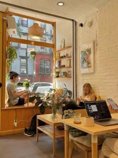 two people sitting at a table with laptops in front of them, looking out the window