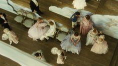 an aerial view of people dressed in formal wear on a wooden floor with chairs and paintings behind them