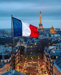 the flag of france is flying high in the sky over an urban area at dusk