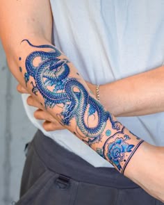 a woman's arm with a blue dragon tattoo on her left arm and wrist