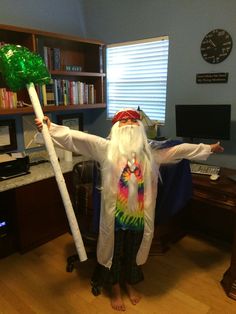 a man dressed as an old wizard holding a green wand and standing in front of a computer desk