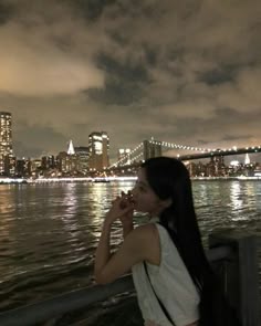 a woman standing on the side of a river next to a large city at night