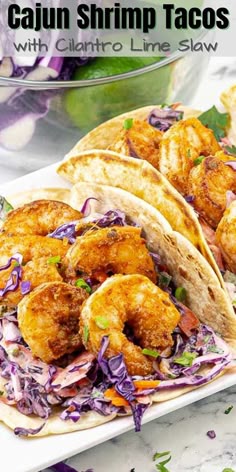 two shrimp tacos on a plate with coleslaw and limes in the background
