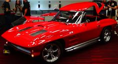 a red sports car is on display in a showroom with people looking at it
