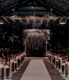 an indoor wedding venue with candles and flowers on the aisle, surrounded by greenery