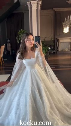 a woman in a wedding dress taking a selfie with her cell phone while standing on the floor