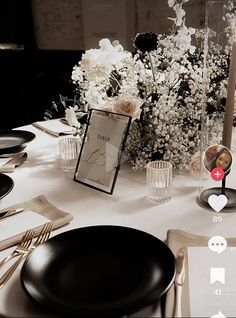 the table is set with black plates, silverware and white flowers in vases