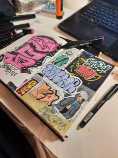 an open notebook sitting on top of a table next to a laptop computer and marker pens