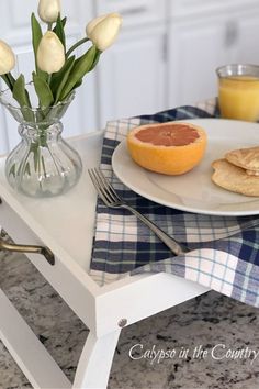 a white plate topped with an orange next to a vase filled with tulips