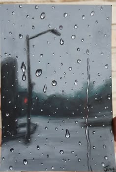 a person holding up a piece of art that has rain drops on it and a street light in the background