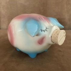 a ceramic piggy bank with a cork sticking out of it's mouth on a brown surface