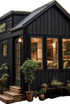 a small black house with lots of windows and potted plants on the front porch