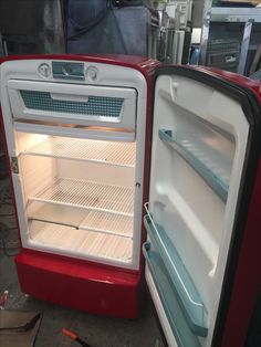 an open red and white refrigerator sitting inside of a kitchen next to another empty fridge