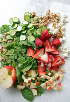 sliced strawberries, cucumbers, and spinach are arranged on a cutting board