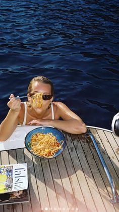 a woman laying on top of a wooden boat eating spaghetti off of her face while wearing sunglasses