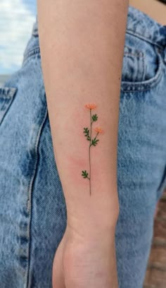 a small flower tattoo on the left inner arm and wrist, with orange flowers growing out of it