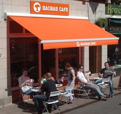 people sitting at tables outside of a cafe with an orange awning