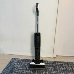 a black and silver vacuum sitting on top of a rug next to a white wall
