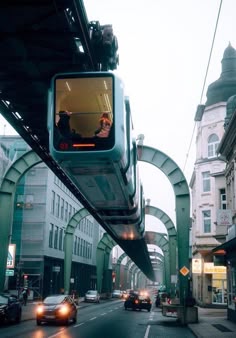 a train going over a bridge with cars on the road and buildings in the background