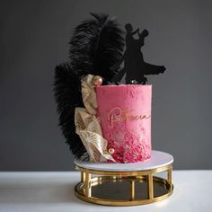 a pink and gold wedding cake with a black silhouette on top, surrounded by feathers