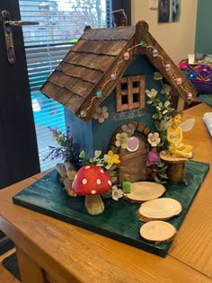 a small house made out of wood with flowers and mushrooms on the roof is sitting on a table