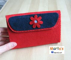 a hand is holding a red and blue felt case with a flower on the front