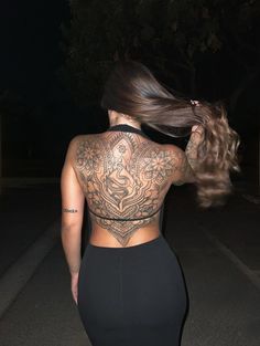 a woman with tattoos on her back walking down the street